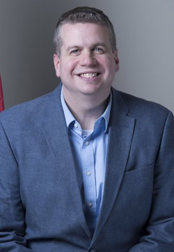 A head and shoulders photo of a man with a grey background