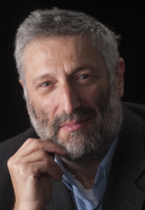 A man with gray hair and a beard leaning on his fist and looking at the camera