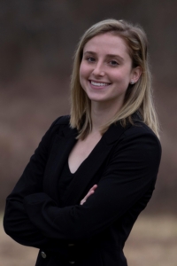 A blonde woman in a black shirt with her arms folded, smiling at the camera