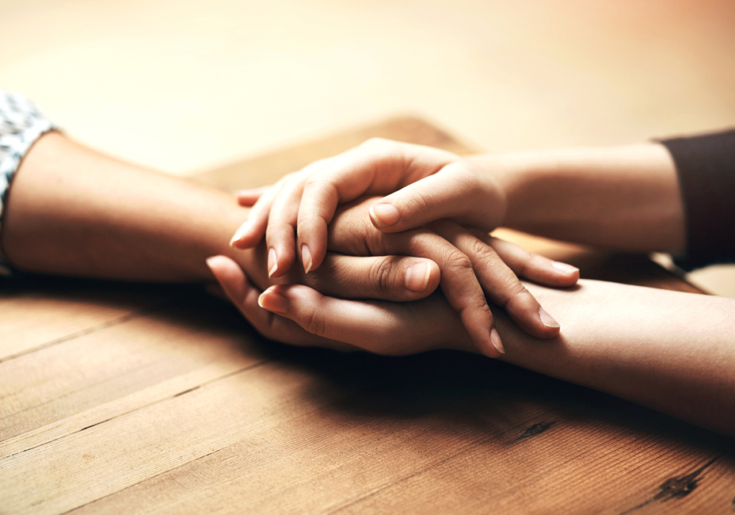 Holding hands, cancer and support of friends, care and empathy together on table in home mockup. Kindness, love and women hold hand for hope, trust or prayer, comfort or compassion, help or unity. A photo of hands, one person holding another person's hand with both of their hands