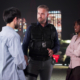 Three people talking, one of them is a man with a badge.