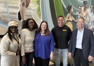 Five smiling people in front of a mural