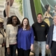 Five smiling people in front of a mural